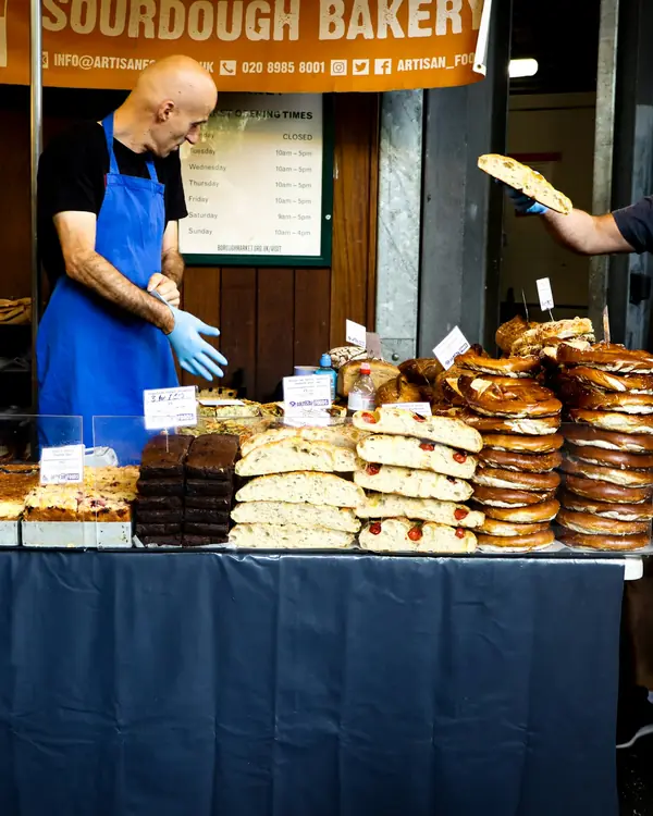 A baker hands pastries across a busy market stall.