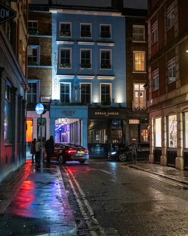 A wet London street at night, lit by shop windows and street lamps.