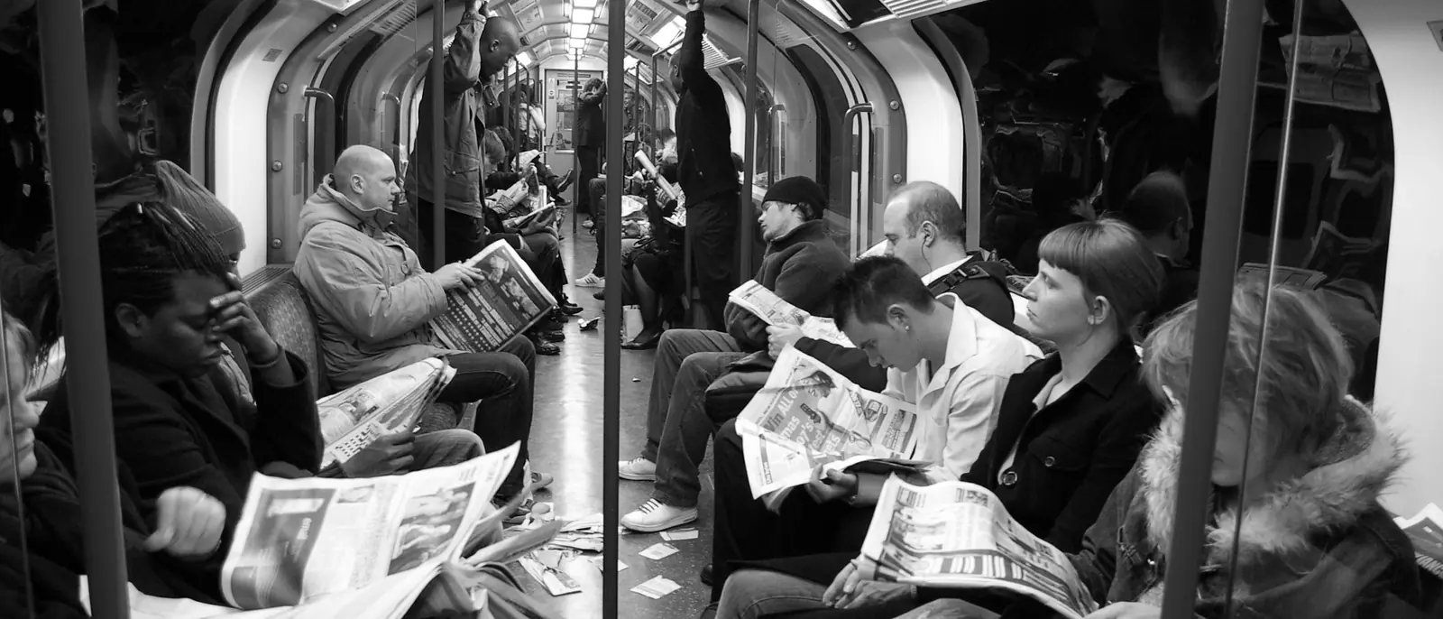Passengers reading newspapers on a London Underground carriage, in black and white.